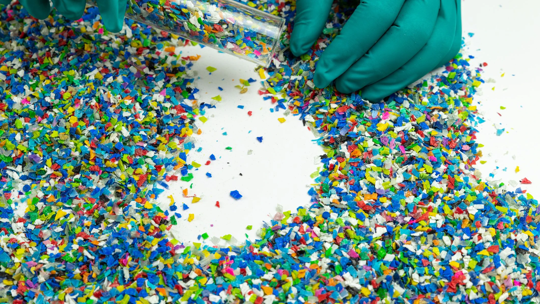 Crushed plastic on green gloved hand. Reuse of plastic. polymer beads. Scraps obtained from plastic waste. The world's plastic reduction policy. Scraps plastic on white background.