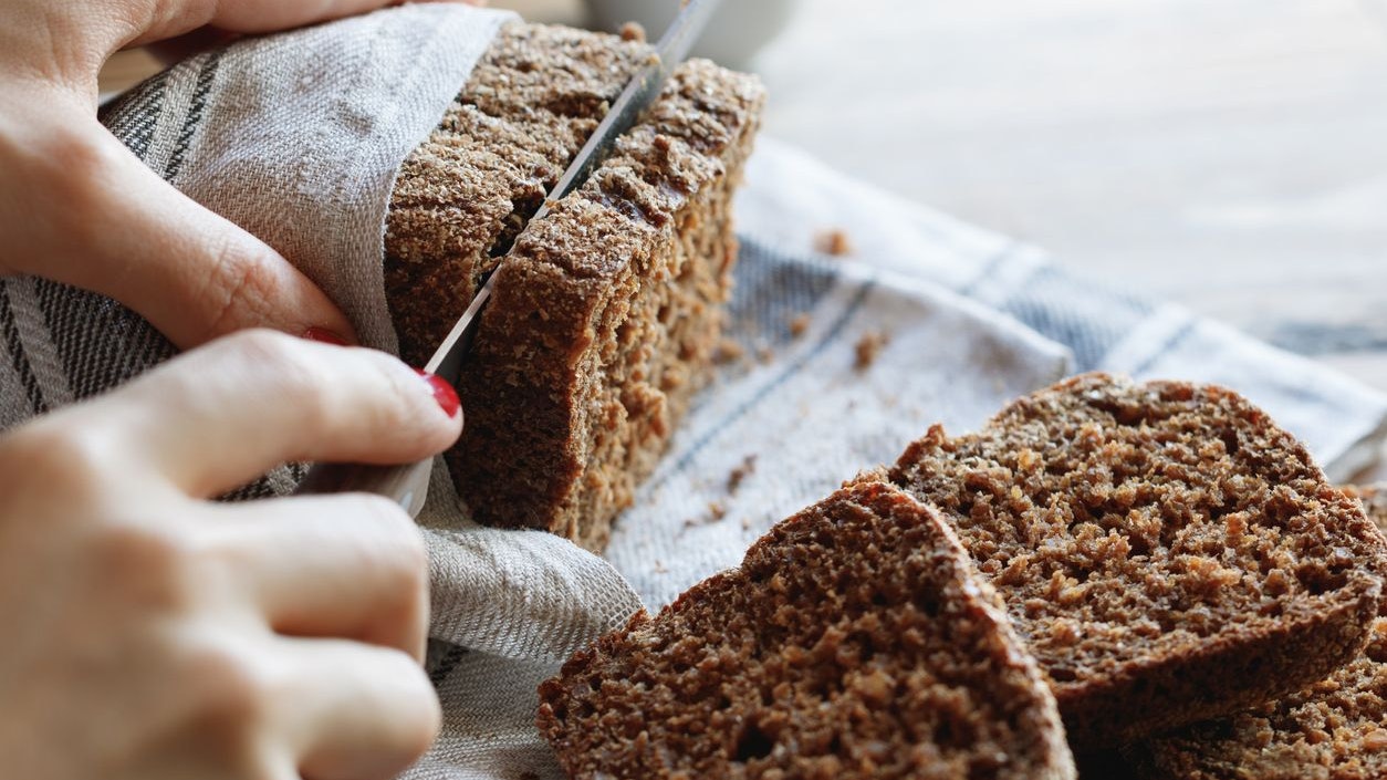 The girl cuts whole-wheat rye bread on a wooden table.