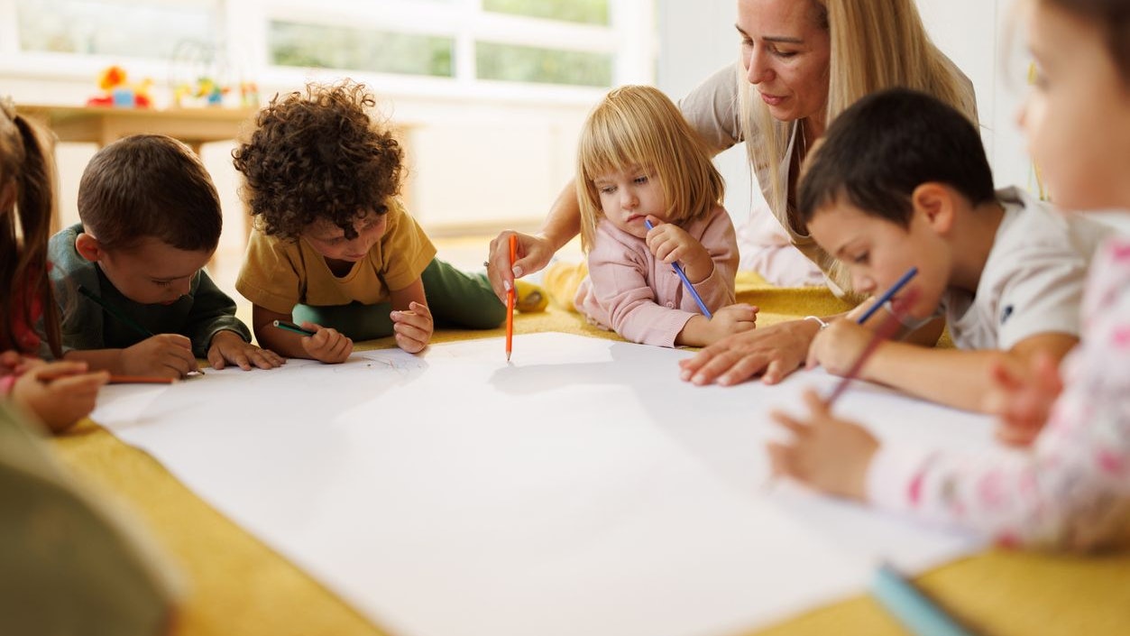 Group of cute little children draw together with their kindergarten teacher