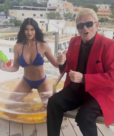 Micaela Schäfer wirbt für den Song im blauen Bikini in einem aufblasbaren Pool – während der 86-Jährige sein Lied neben ihr trällert.