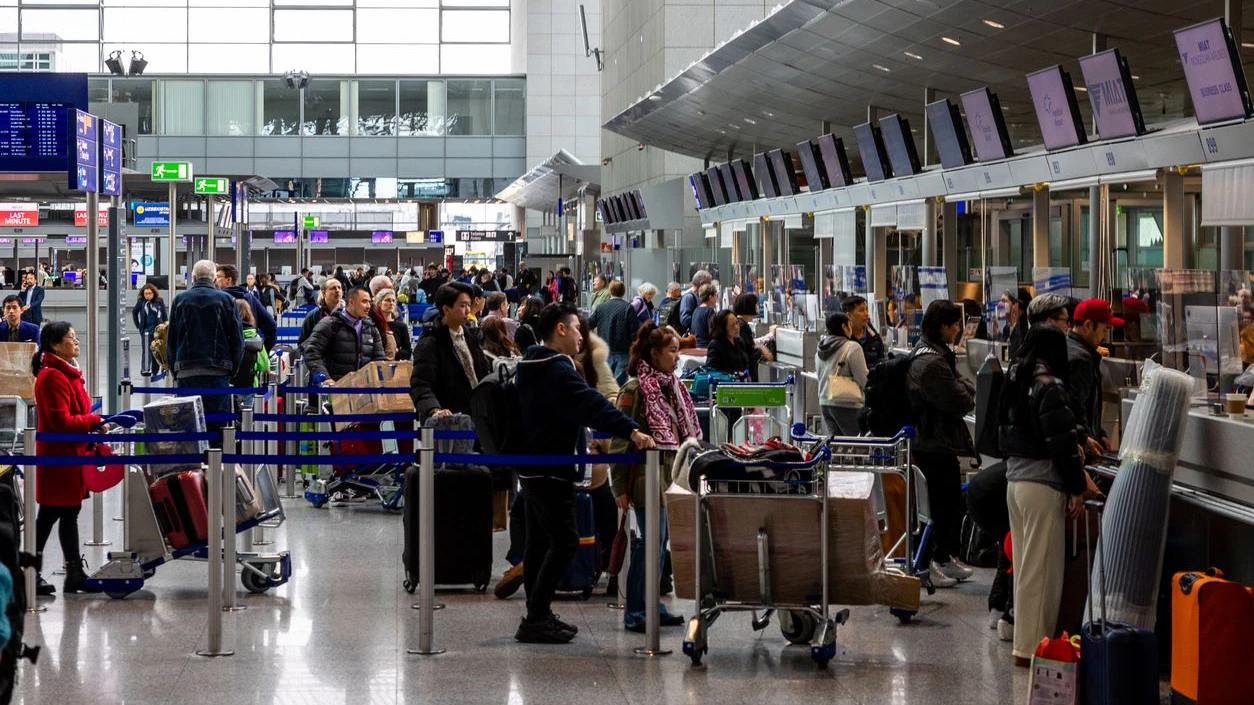 Frankfurt Airport, Germany - February 19, 2024: the image depicts a bustling airport check-in counter with numerous travelers waiting in line, pushing luggage carts, and interacting with airline staff. The scene is filled with bags, suitcases, and people, reflecting the typical commotion of a busy airport.