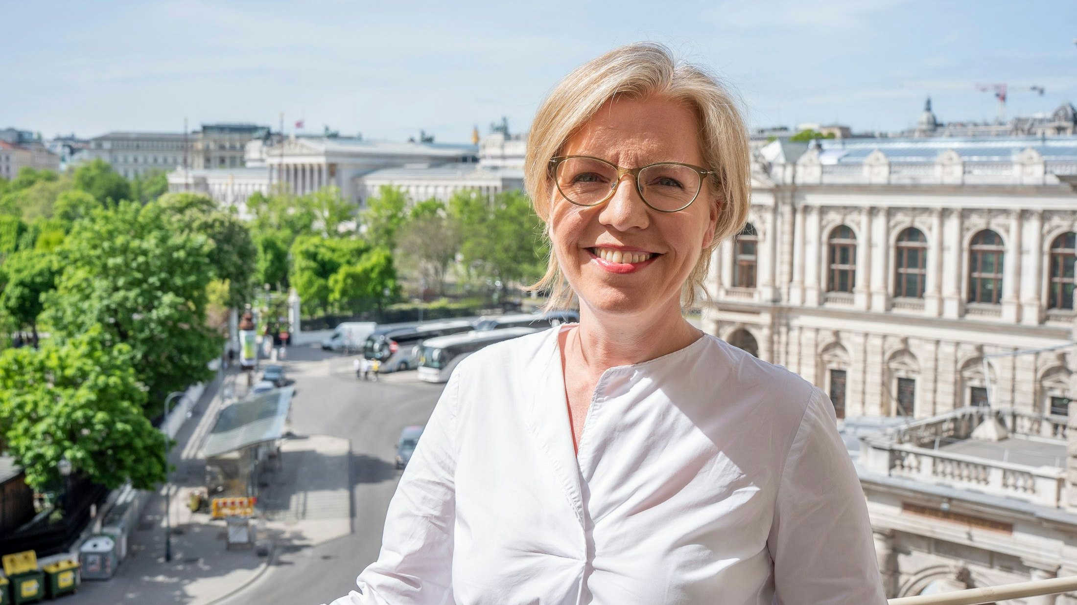 Leonore Gewessler am Büro-Balkon des Grünen Klubs mit Blick auf Burgtheater und Parlament.