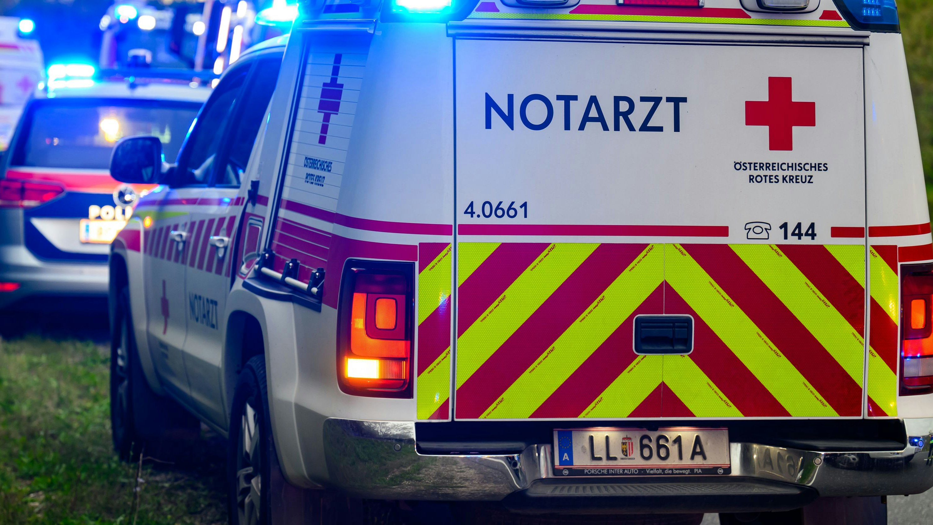 Download von www.picturedesk.com am 23.04.2025 (11:20).  Auf dem Bild ist ein Notfalleinsatz am Straßenrand zu sehen. Ein Rettungswagen mit der Aufschrift "Notarzt" vom Österreichischen Roten Kreuz steht am Einsatzort mit eingeschaltetem Blaulicht. Im Hintergrund sind weitere Rettungs- und Polizeifahrzeuge sowie Feuerwehrleute zu erkennen, die offenbar an einem Unfallort tätig sind. Aufgenommen am 8. Oktober 2024 - 20241008_PD16957 - Rechteinfo: Rights Managed (RM)