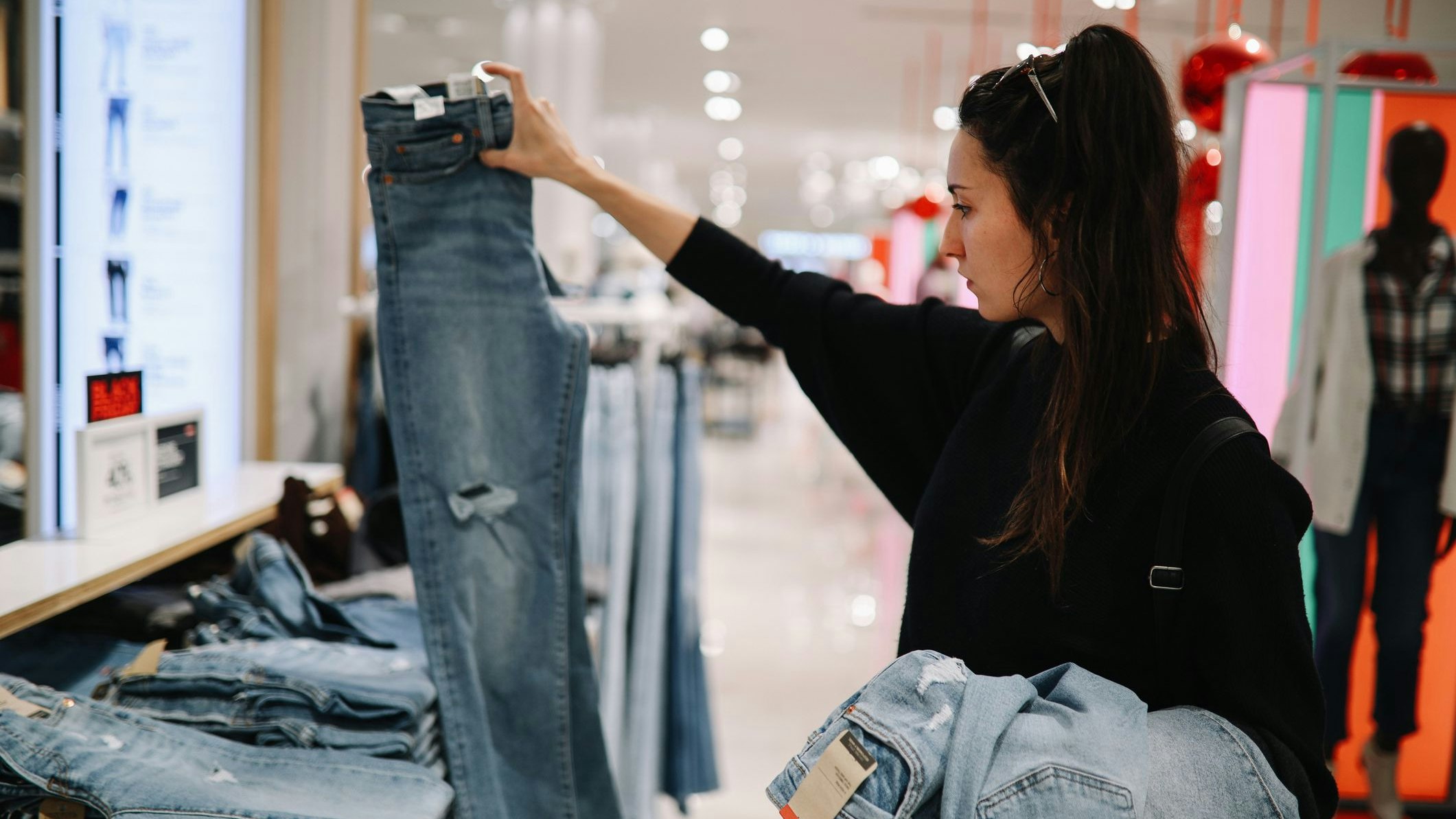 Woman in mid 30s goes shopping for denim jeans in a mall or a clothing store.