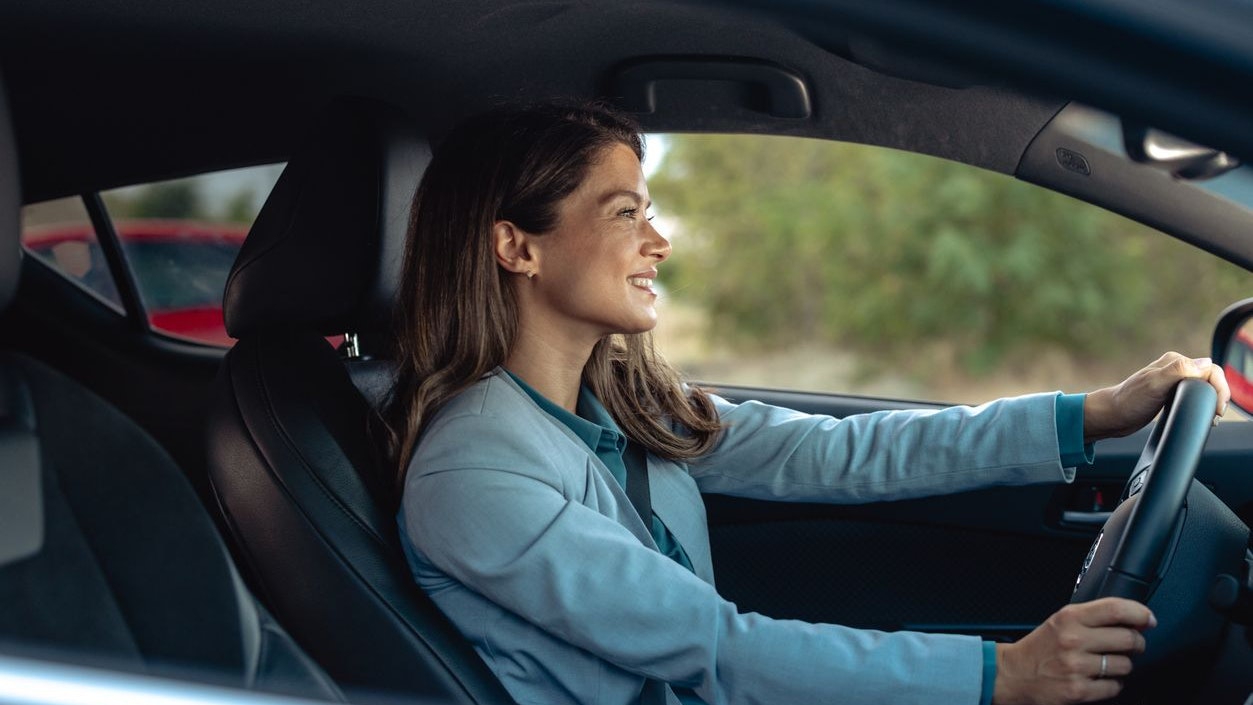 A professional mid-adult woman confidently driving a modern car in an urban setting, showcasing independence and a modern lifestyle.