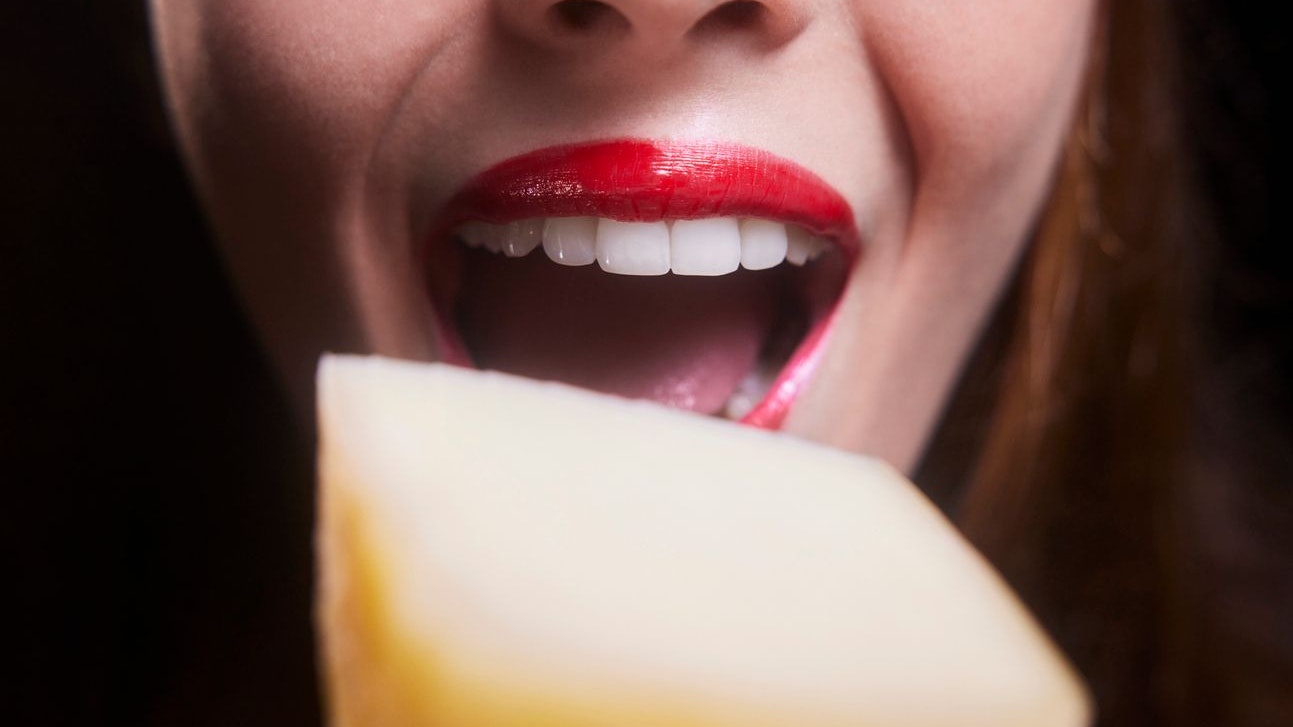 Close-up of young woman mouth biting piece of cheese