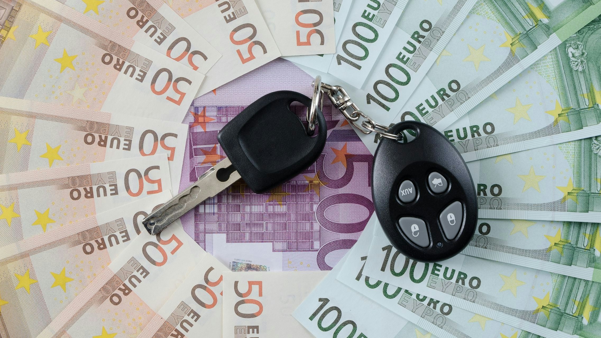 Different euro banknotes and car key lying on a table.