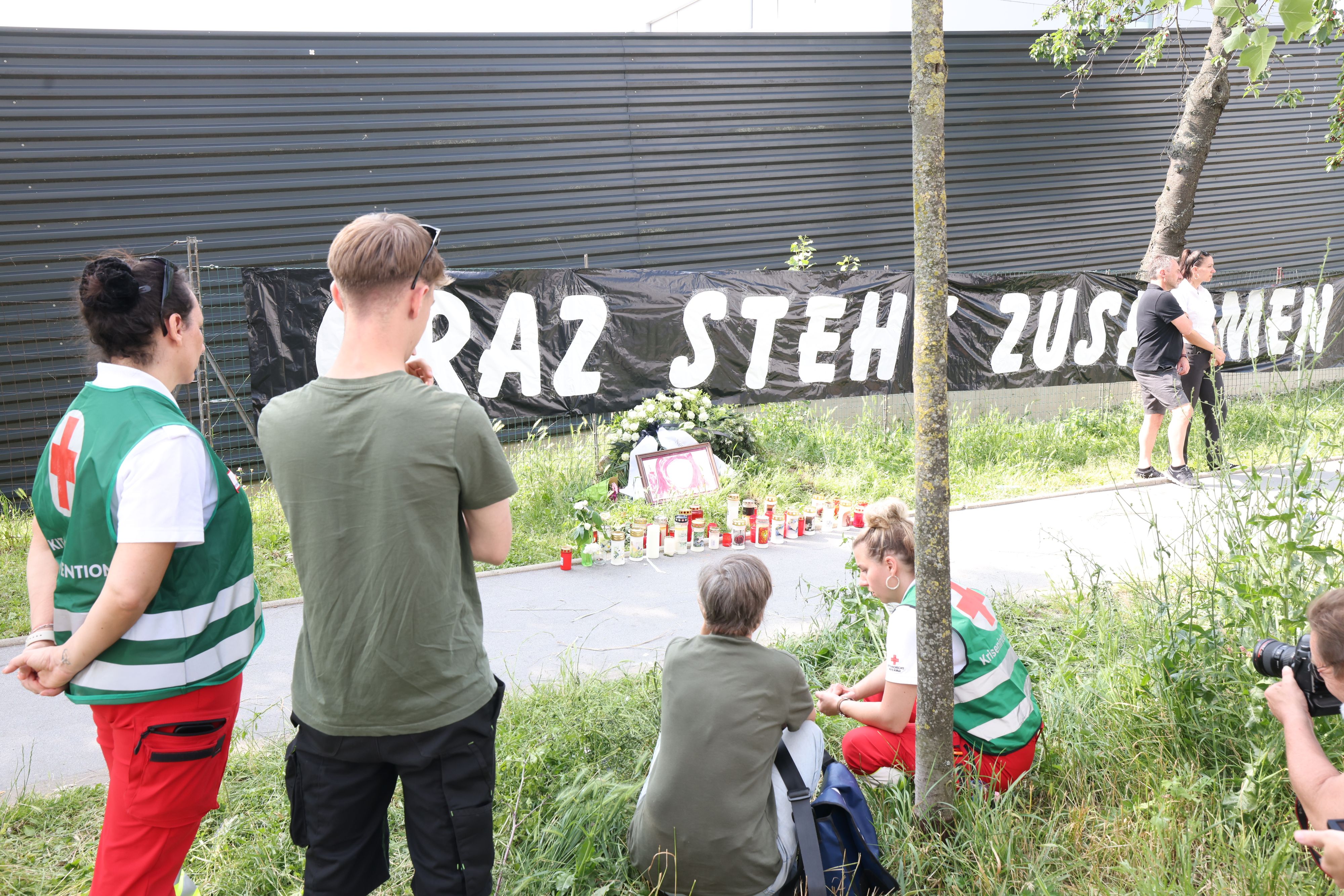 Schüler stehen vor Blumen und Kerzen, die von Angehörigen der Opfer vor dem Schulzaun aufgebaut wurden.