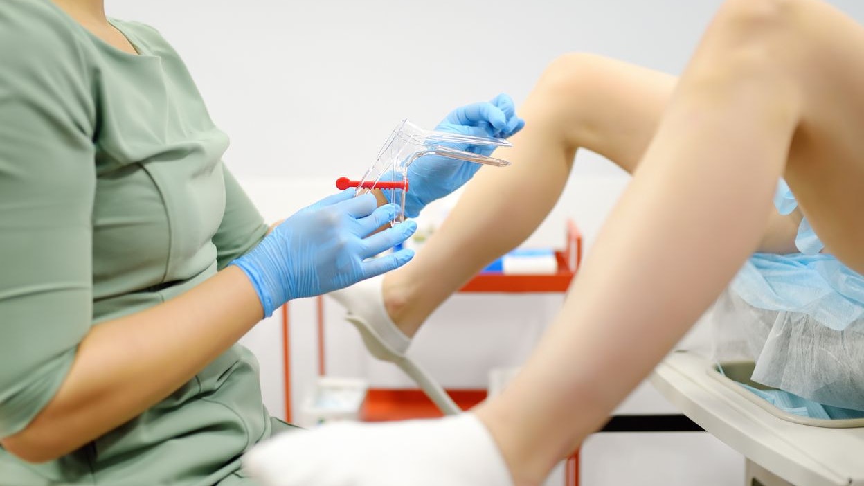 Gynecologist examines a patient laying on gynecological chair using medical vaginal speculum. Doctor takes a smear from a young woman cervix. Diagnosis of diseases. Woman reproductive health.
