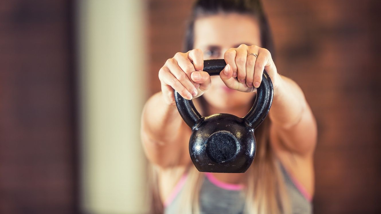 Attractive woman with slim body in gym holding a kettlebell.