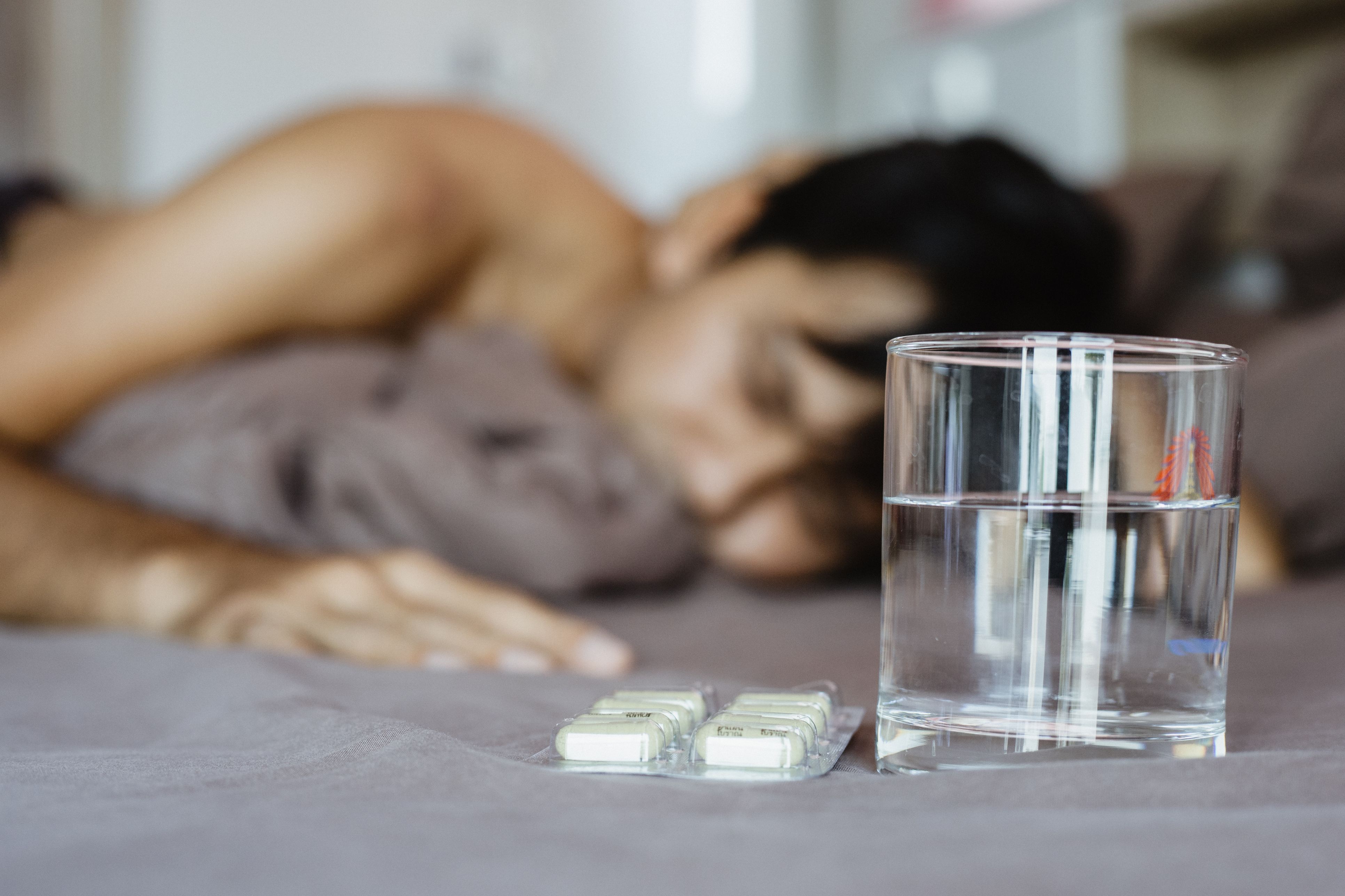 Close-up of pills and glass of water on bed and man sick sleeping on bed