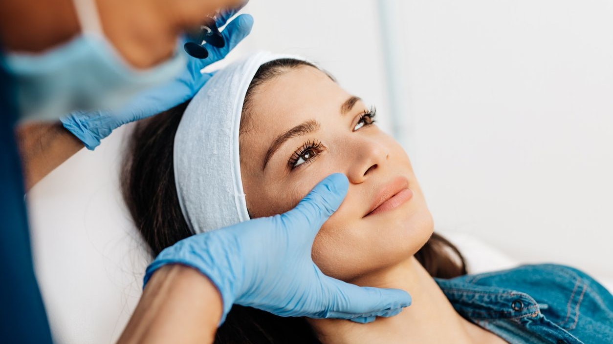 Attractive young woman is getting a rejuvenating facial injections at beauty clinic. The expert beautician is filling female wrinkles by botulinum.