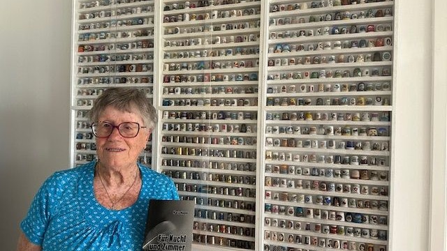 Maria Mayer vor ihrer Fingerhutsammlung. In der Hand hält sie ihr Gedichtebuch "Für Kuchl und Zimmer".