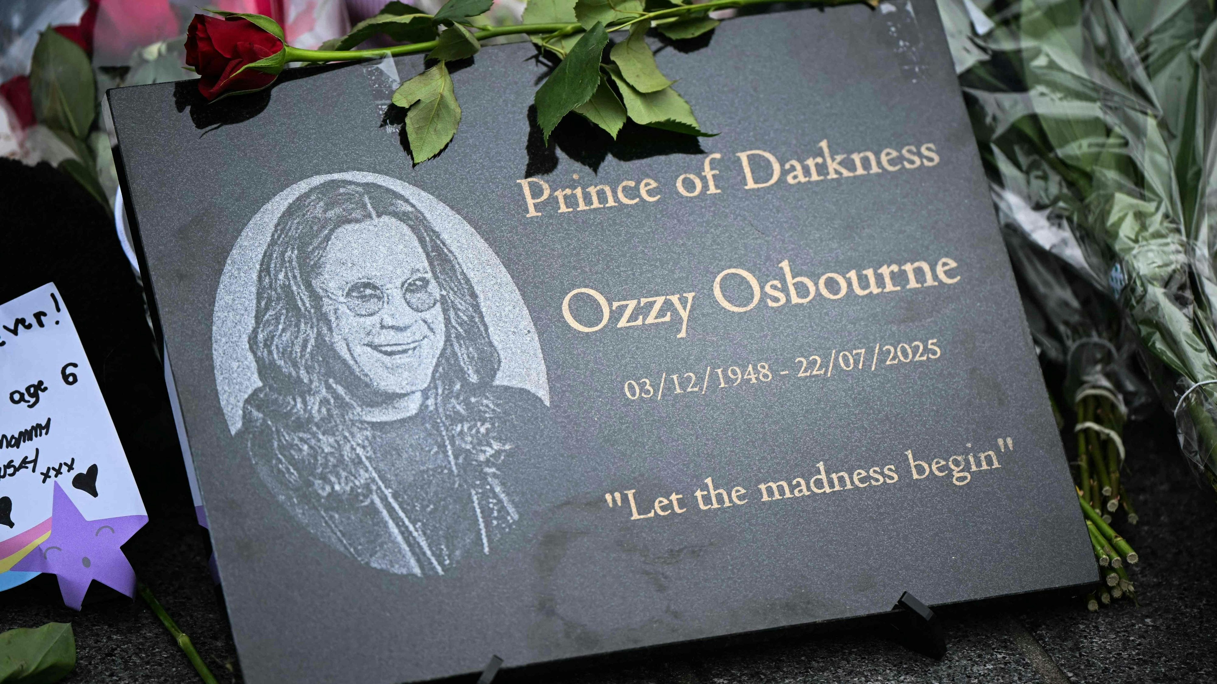 Download von www.picturedesk.com am 30.07.2025 (10:40).  A photograph taken on July 23, 2025 shows a memorial plaque left at a makeshift memorial by a mural depicting late British singer-songwriter Ozzy Osbourne, in Birmingham, central England, a day after his death. Tributes poured in on July 23, 2025 for hell-raiser singer Ozzy Osbourne as tearful fans laid flowers in his hometown and his Black Sabbath band mates mourned the death of their legendary heavy metal frontman, just weeks after he played an epic farewell concert in their Birmingham hometown. Osbourne, nicknamed the "Prince of Darkness" who famously once bit off the head of a bat while on stage, died on July 22, 2025 at the age of 76, his family said. (Photo by JUSTIN TALLIS / AFP) - 20250723_PD5589 - Rechteinfo: Rights Managed (RM) Nur für redaktionelle Nutzung! Werbliche Nutzung erfordert Freigabe: bitte schicken Sie uns eine Anfrage.