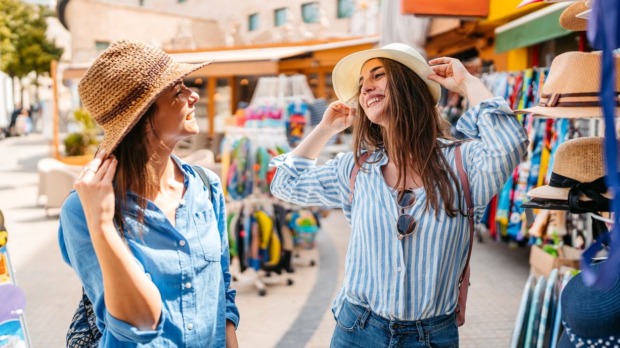 Two young female friends shopping for hats at the street market in Palma de Mallorca, Spain.