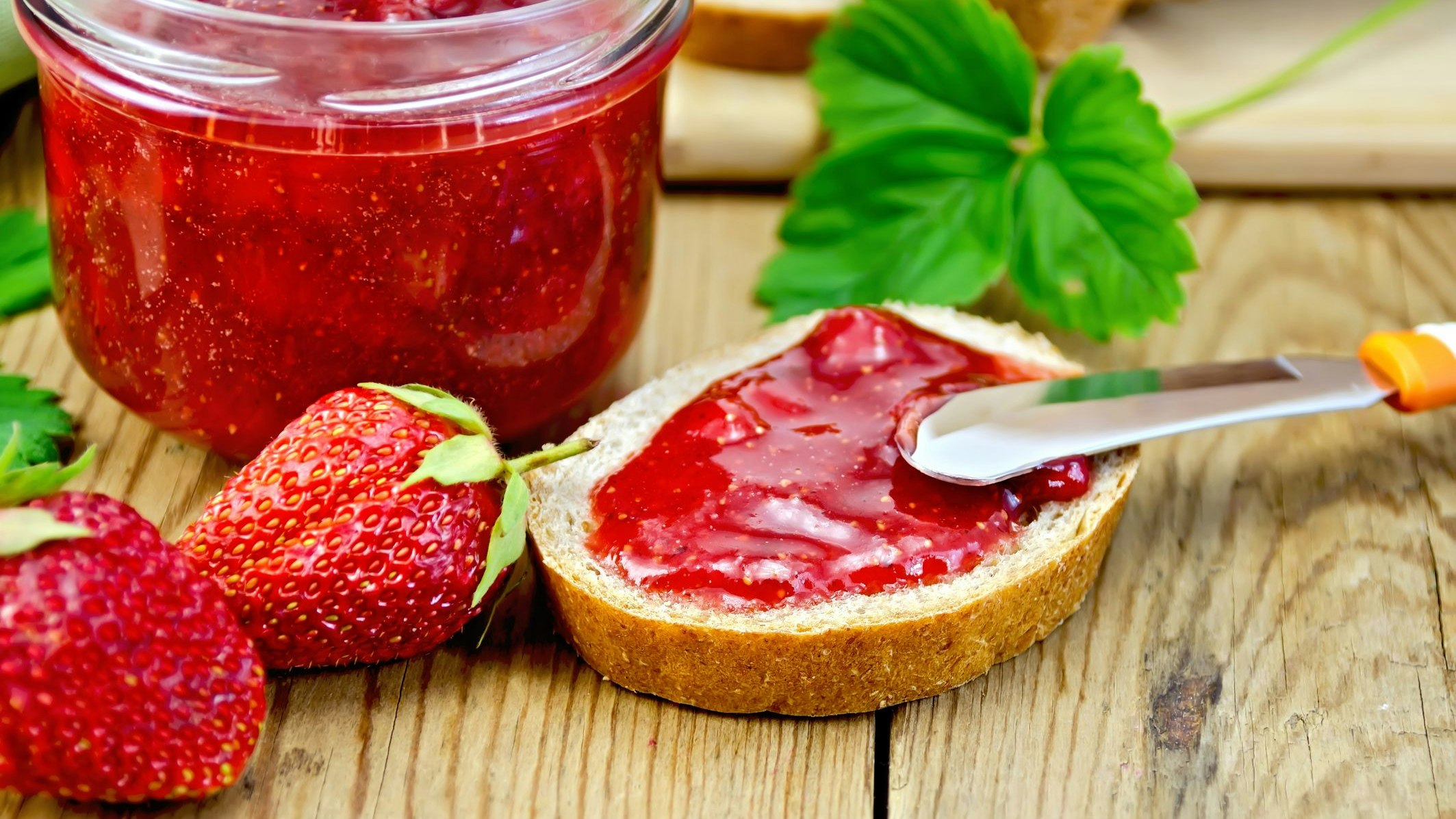 Bread with strawberry jam, a jar of jam, knife, strawberries on a wooden boards background