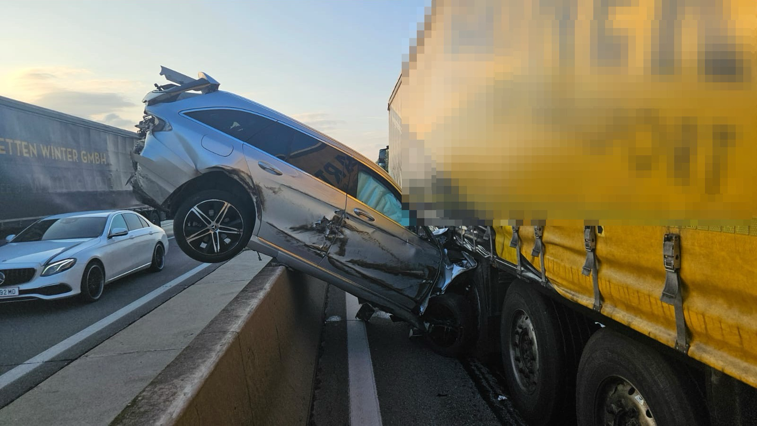 Spektakulärer Unfall: Pkw zwischen Lkw und Mittelleitschiene eingeklemmt