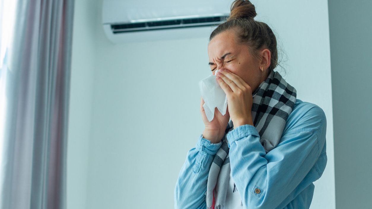Sick sneezing woman caught a cold from the air conditioner at home