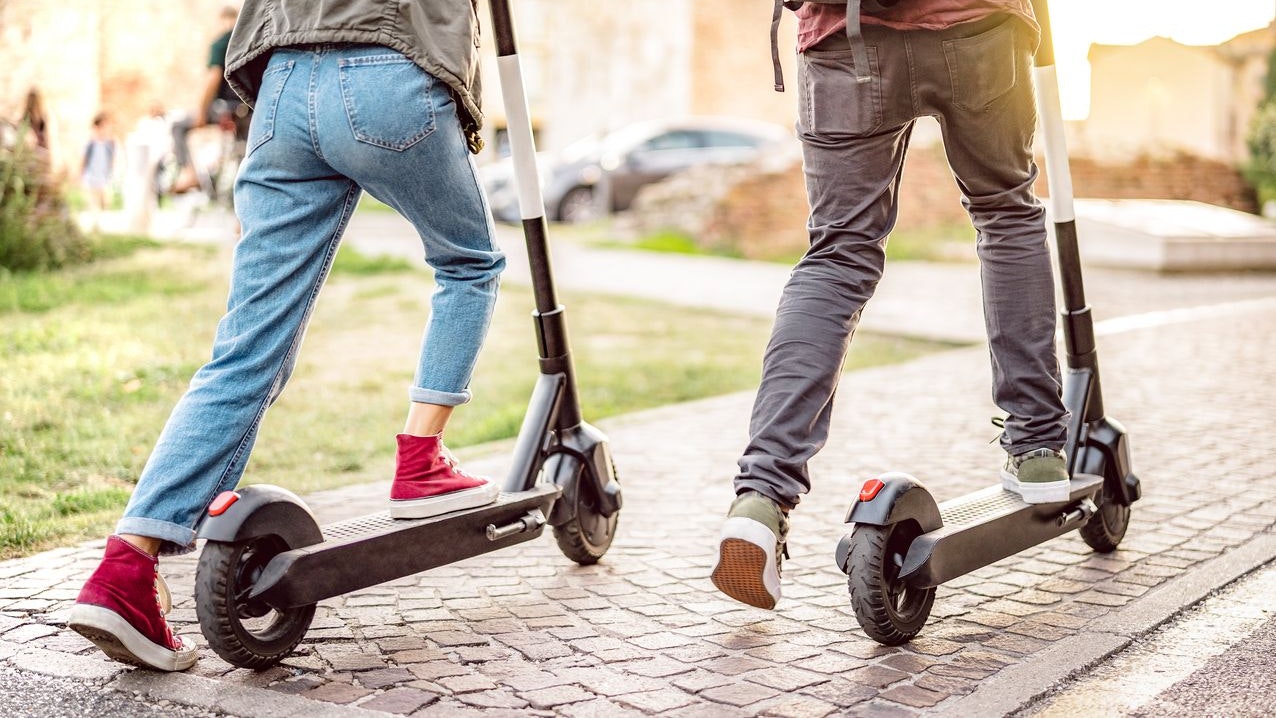 Millenial couple riding electric scooters at urban city park - Genz students using new ecological mean of transportation - Green eco energy concept with zero emission - Warm filter with sunshine halo