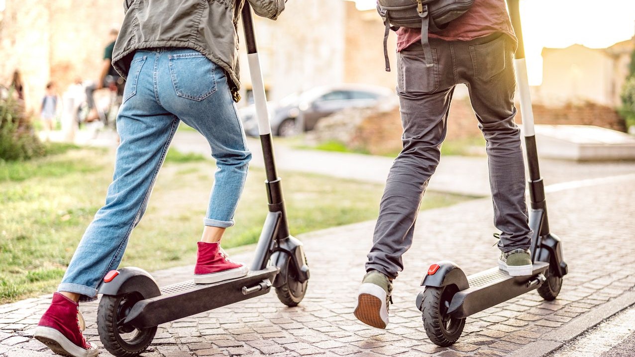 Millenial couple riding electric scooters at urban city park - Genz students using new ecological mean of transportation - Green eco energy concept with zero emission - Warm filter with sunshine halo