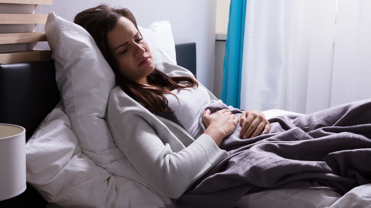 Young Woman Lying On Bed Suffering From Stomach Pain