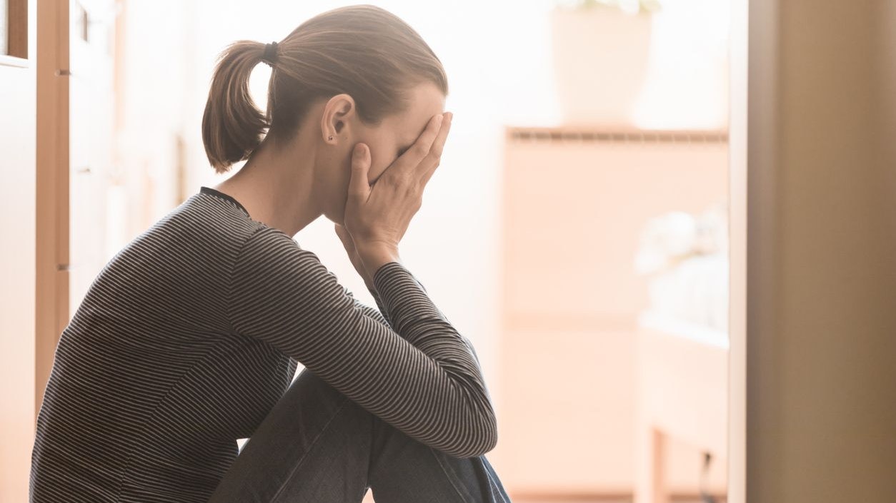 Young woman feeling sad siting at home on the floor.