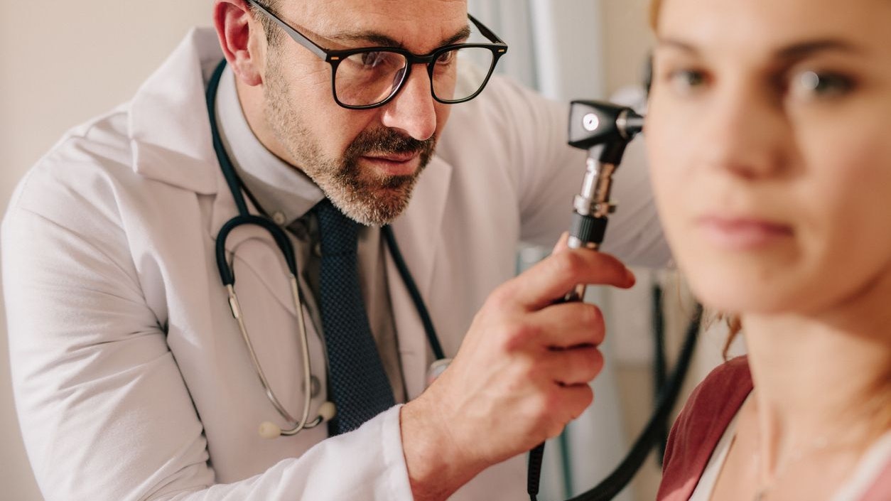 ENT doctor checking ear with otoscope of woman patient at hospital. Physician examining ear of female patient with an instrument.