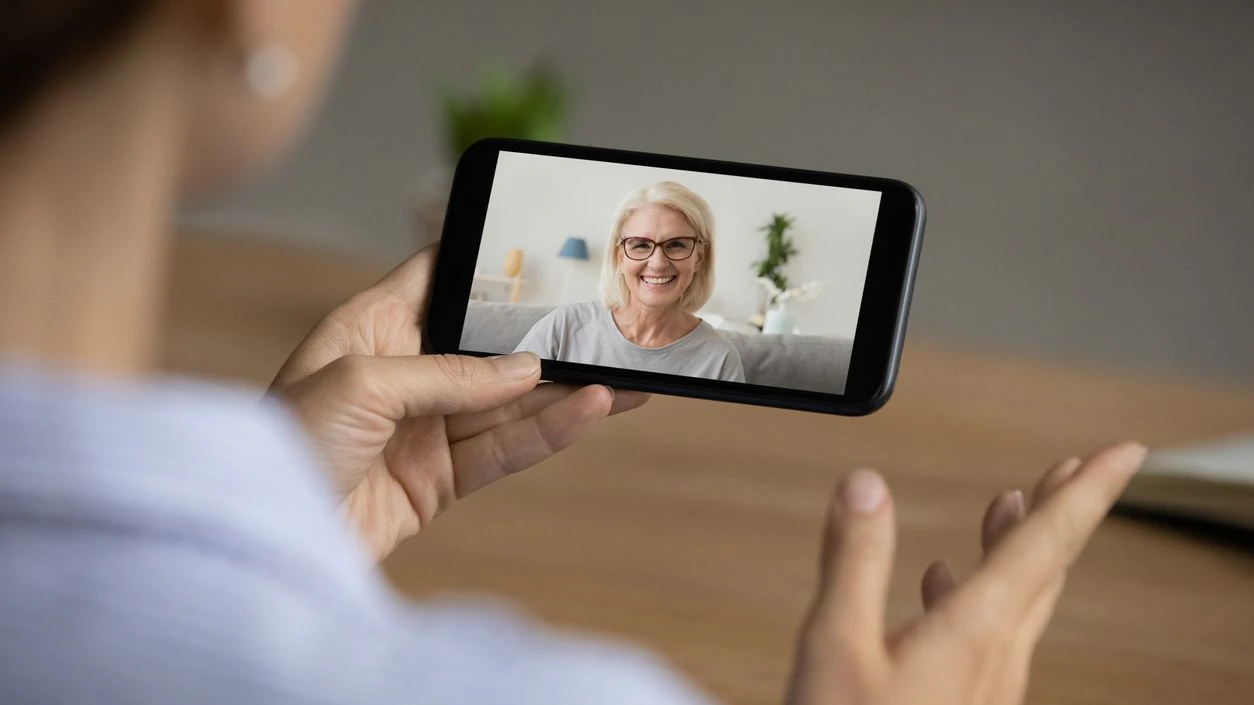 Back view of woman talk speak on video call on smartphone gadget with smiling elderly Caucasian mom. Female have webcam digital online conversation on cellphone with mother. Communication concept.