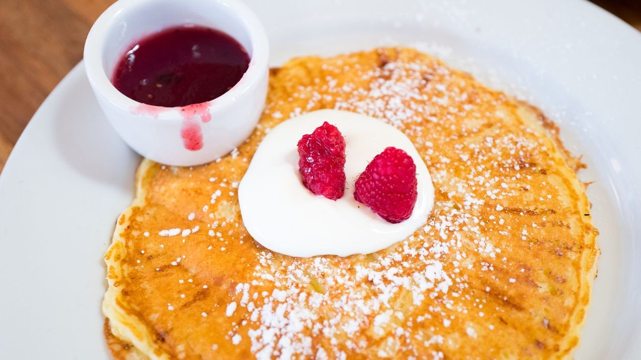 Close-up of ricotta pancakes with raspberries and creme fraiche, with raspberry sauce, on a white plate, February 25, 2018