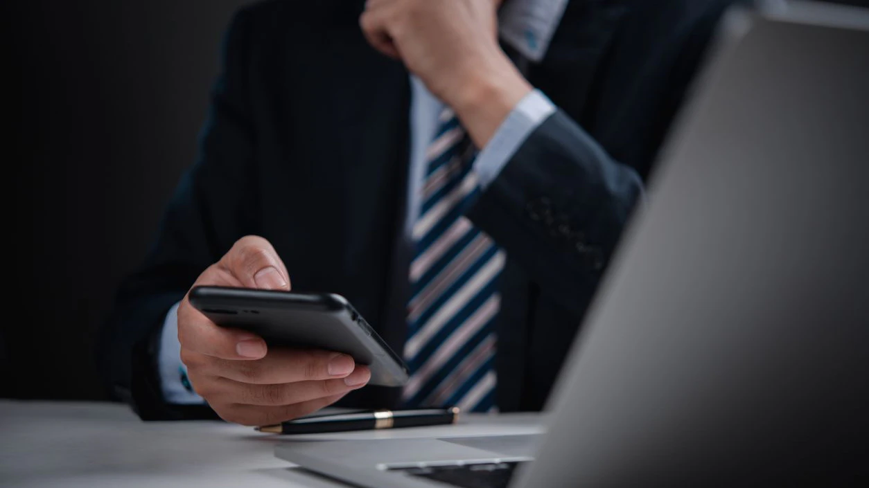 Corporate leader holding phone with pen and laptop, great for concepts of business thinking, fintech, and remote leadership.