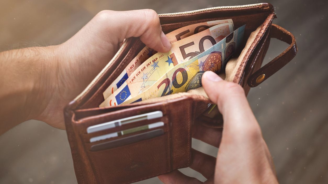 Hands opening a leather wallet with 50 Euro and 20 Euro banknotes inside.