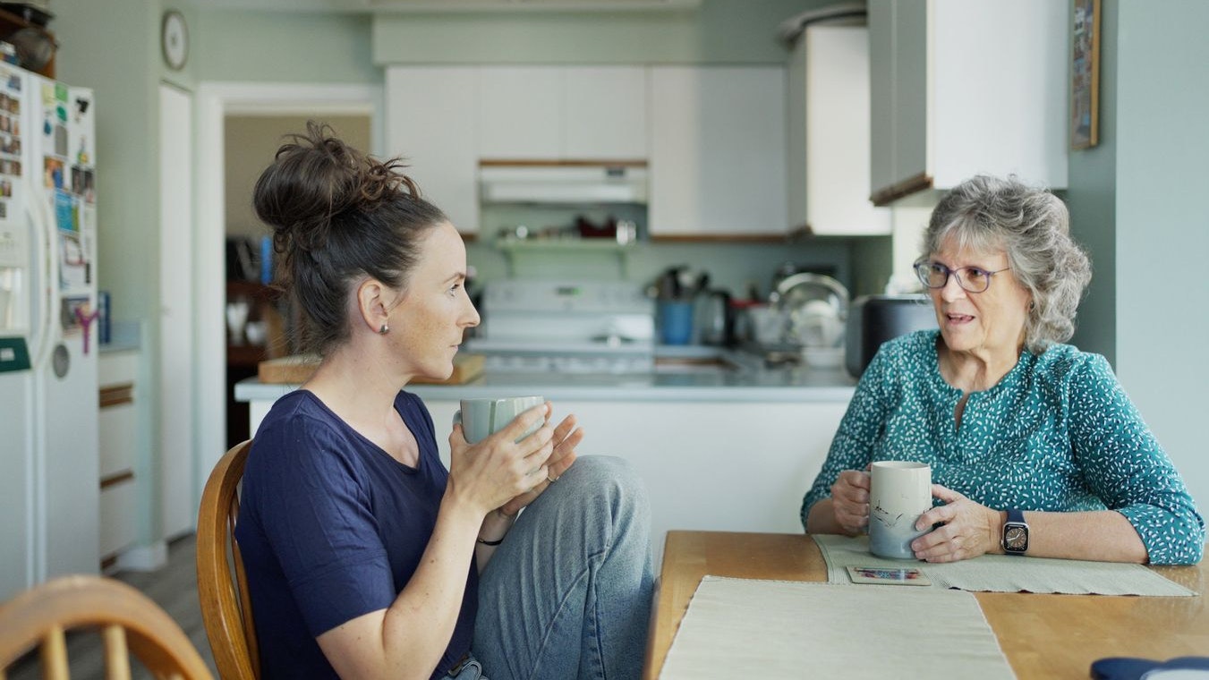 Young woman talking with her mature mother over tea at a kitchen table at home during a visit