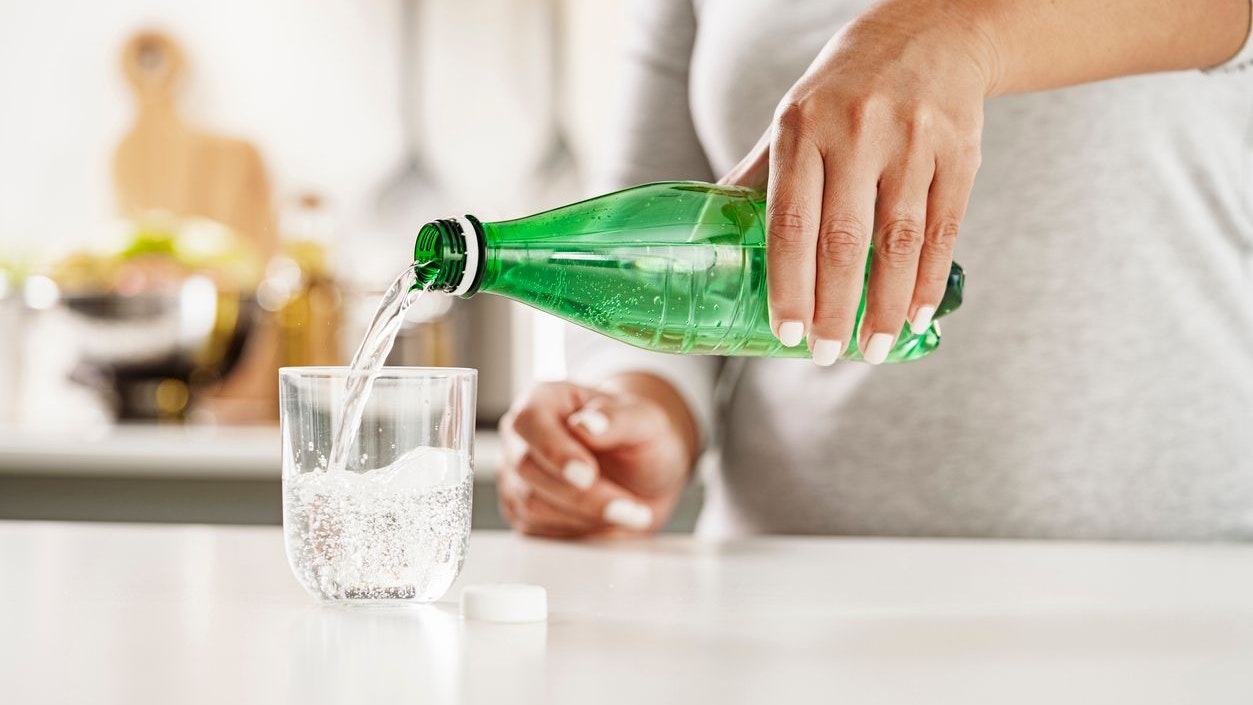Close up view of female hands pouring tonic water from a green plastic bottle to a glass on kitchen counter. High resolution 42Mp indoors digital capture taken with Sony A7rII and Sony FE 90mm f2.8 macro G OSS lens