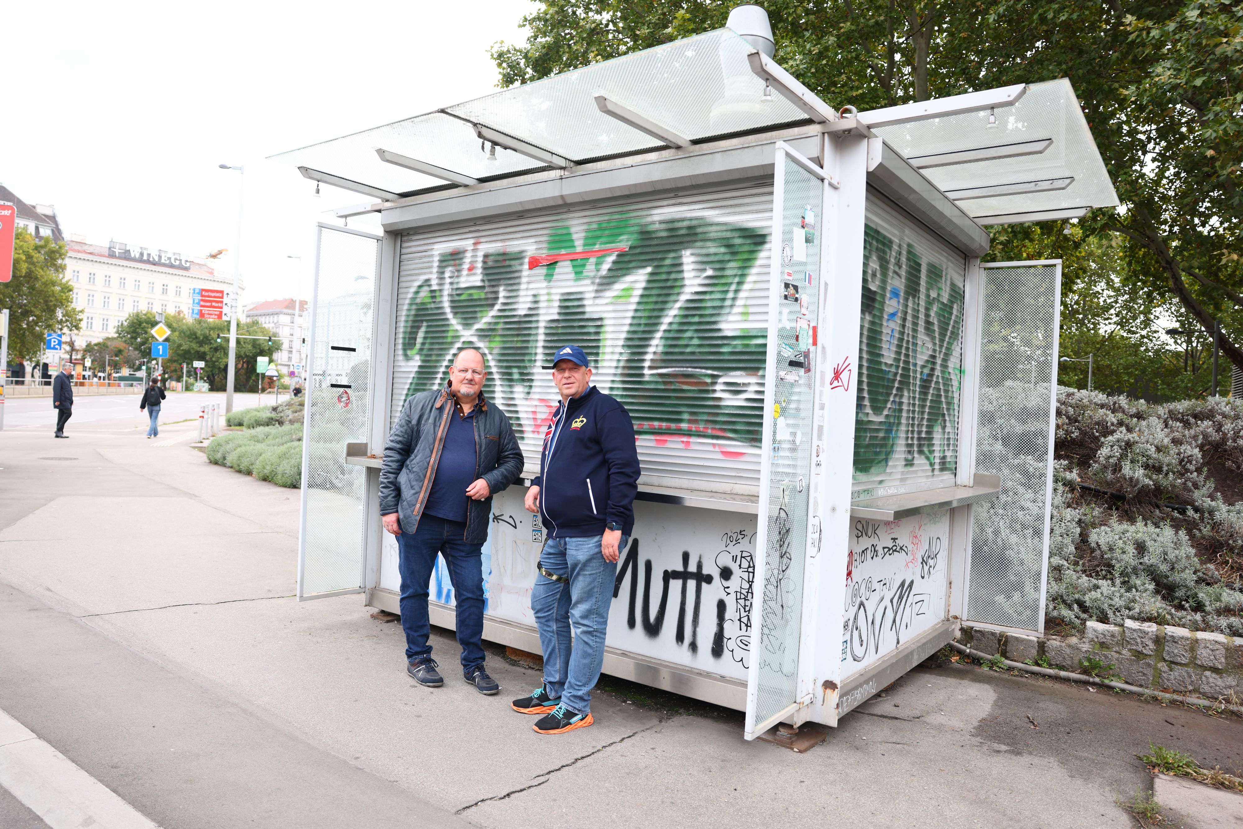 Die Brüder Alexander (54) und Robert Sedlak (59) vor ihrem geschlossenen Würstelstand – nach Jahrzehnten soll das Kult-Standl verkauft werden.