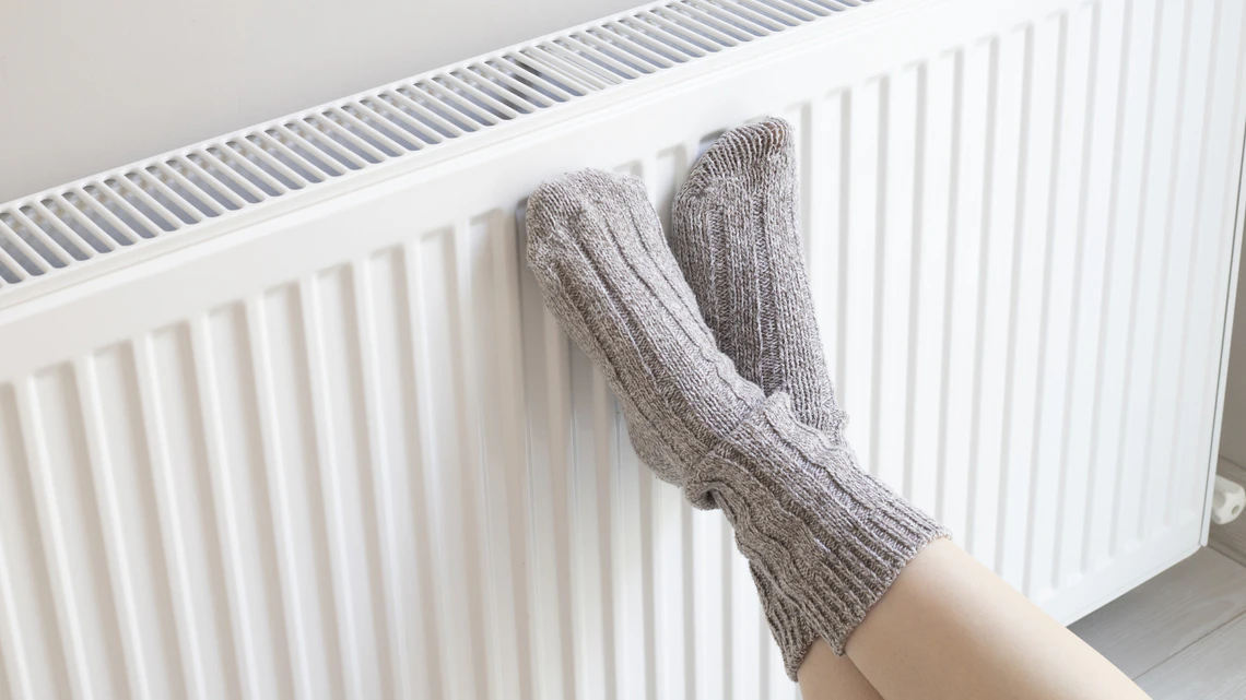 Woman is warm knitted woolen socks near a home heater in cold winter time. Using heater at home in winter.