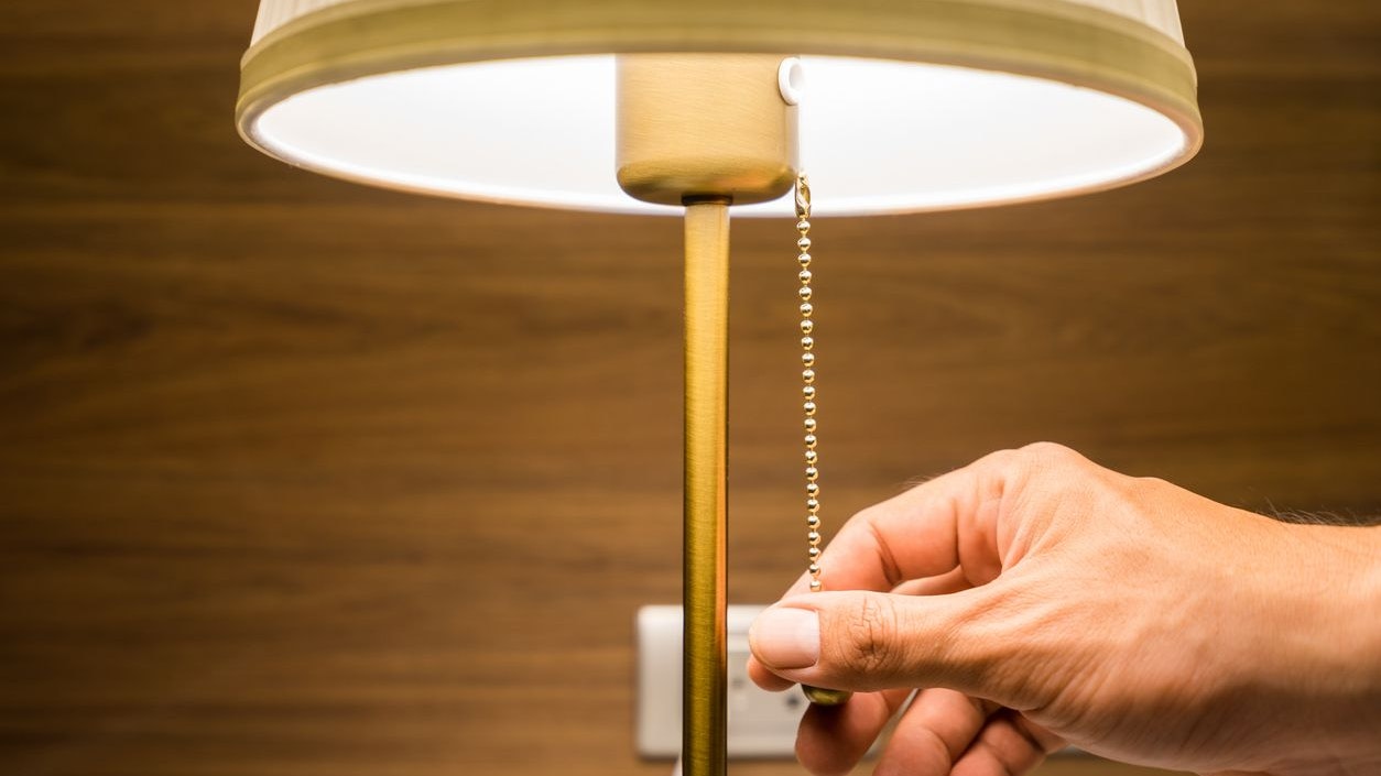 Hand of person is turning on or turning off the bedroom 's head lamp which is beautiful luxury-modern designed. Close up and selective focus photo.