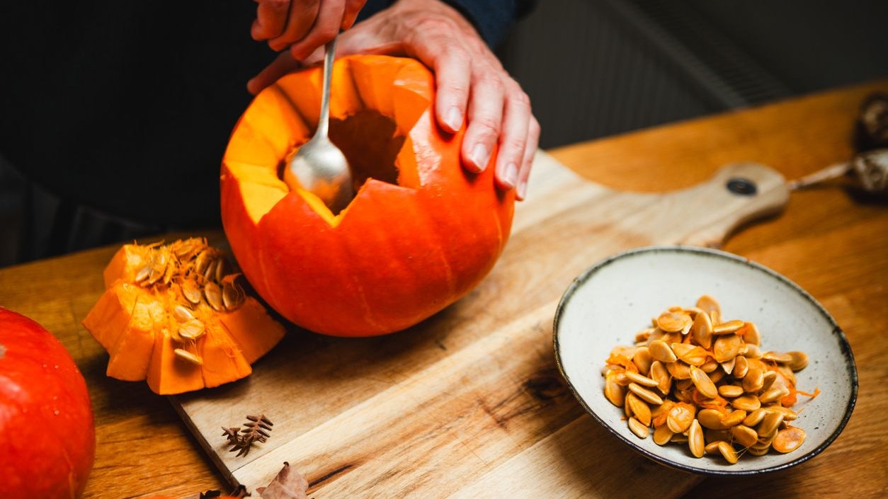 Close-up of man hands taking out seeds from pumpkin with a spoon while carving Jack O Lantern for Halloween. Hands carving a pumpkin Jack O Lantern for Halloween.