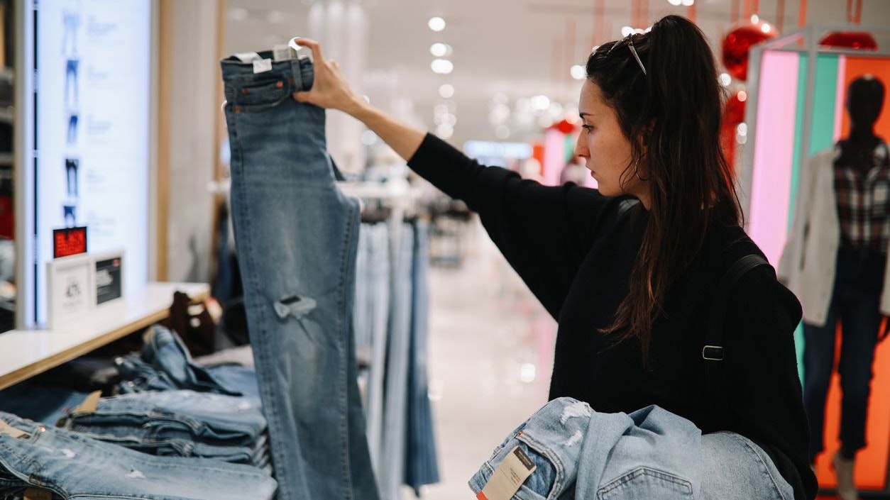 Woman in mid 30s goes shopping for denim jeans in a mall or a clothing store.