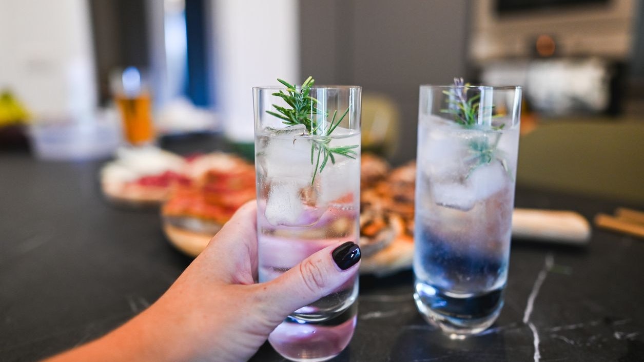 Hand holding a refreshing gin and tonic cocktail with ice and rosemary