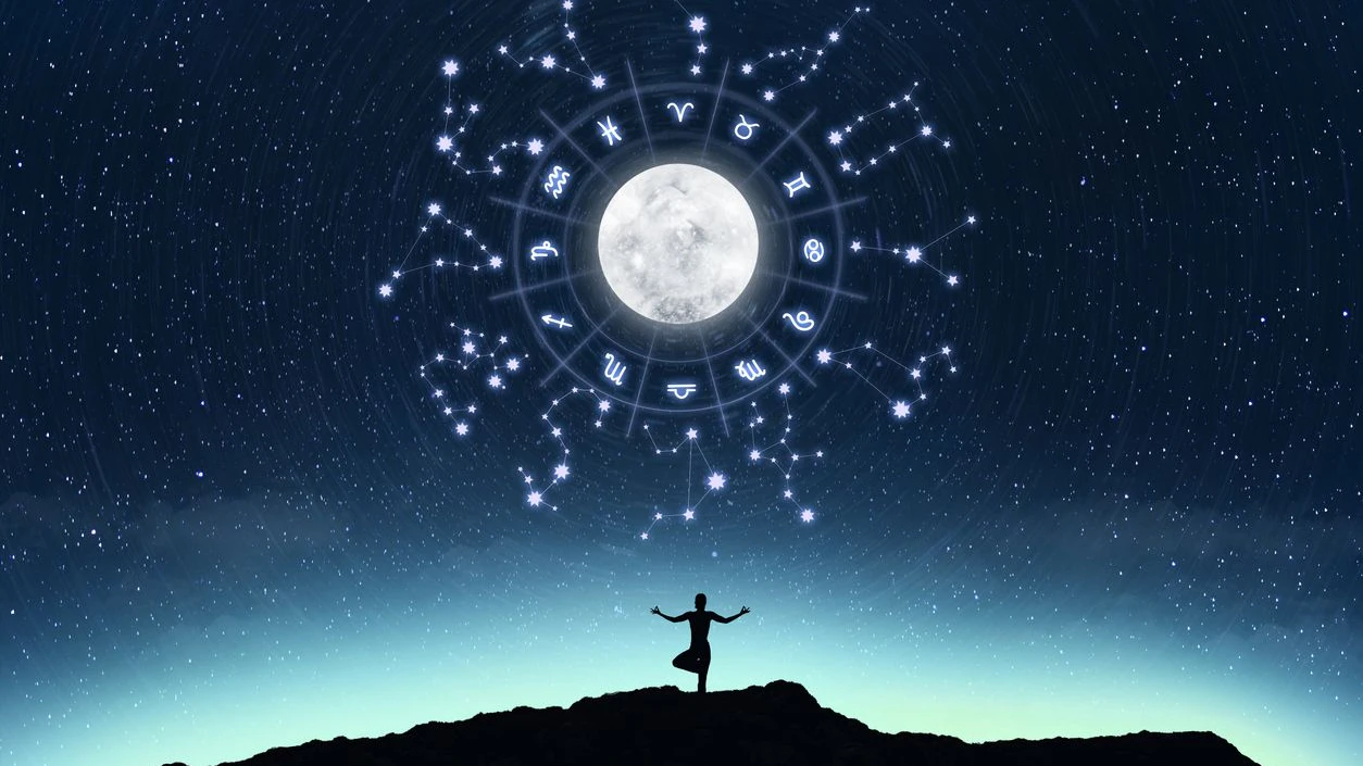 A silhouette of a person gazing at the moon with glowing zodiac symbols and constellations in the night sky.
