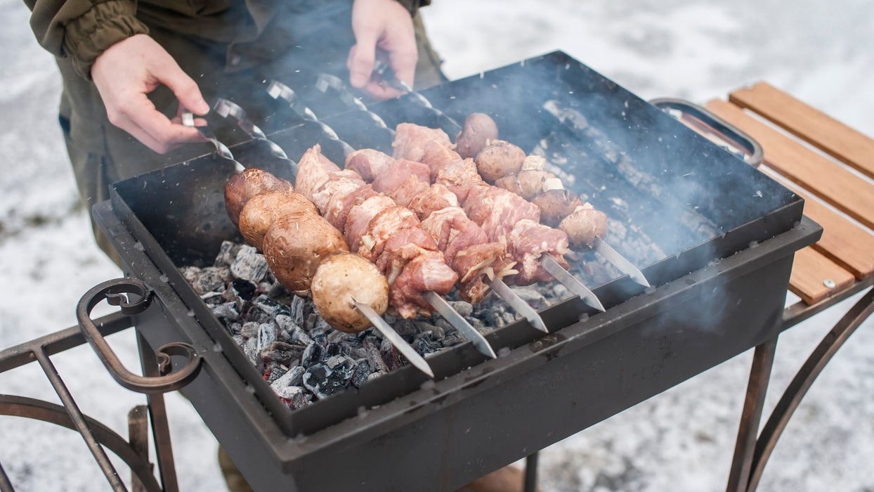 A man grills meat and mushrooms in winter. close-up. Winter picnic, outdoor recreation.