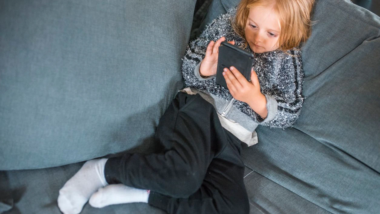 Young blond girl is sitting on the sofa and using mobile phone.