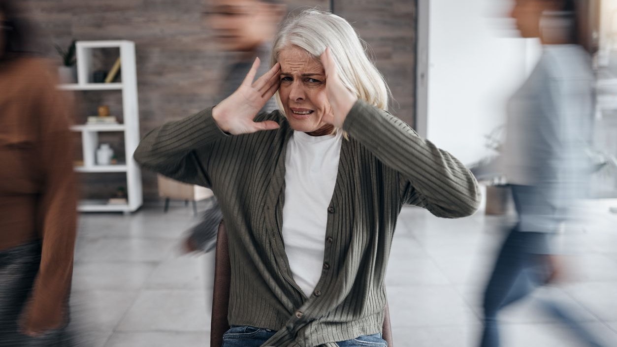 Anxiety, bipolar and woman with mental health problem, focus and psychology crisis in busy office. Stress, depression and burnout or dementia of senior person with fast people, speed or walking crowd