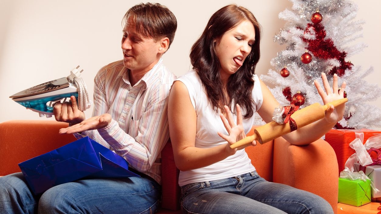 a young couple is sitting on the couch and exchanging christmas gifts. both of them seem quite unhappy with the stuff they got....