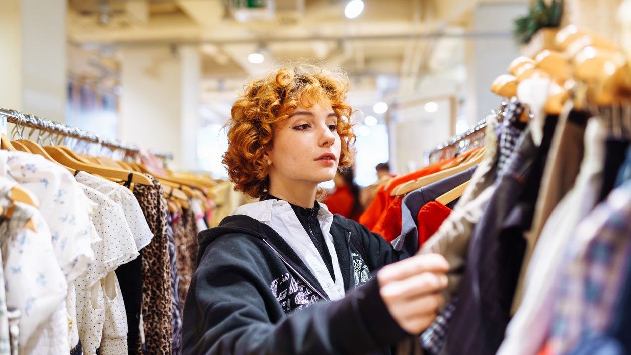 portrait of red-haired attractive young woman trying on clothes in store, buying autumn clothes, shopping