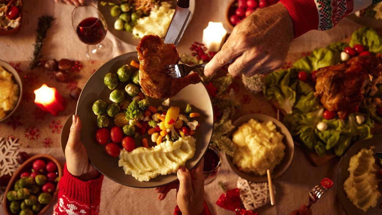 Close up of unrecognizable man serving roasted meat to his wife during dinner at dining table.