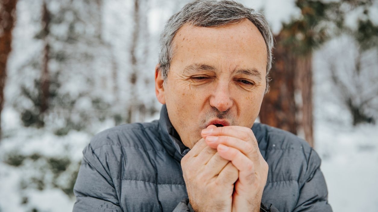 mature man is cold and blowing at his hands trying to warm up