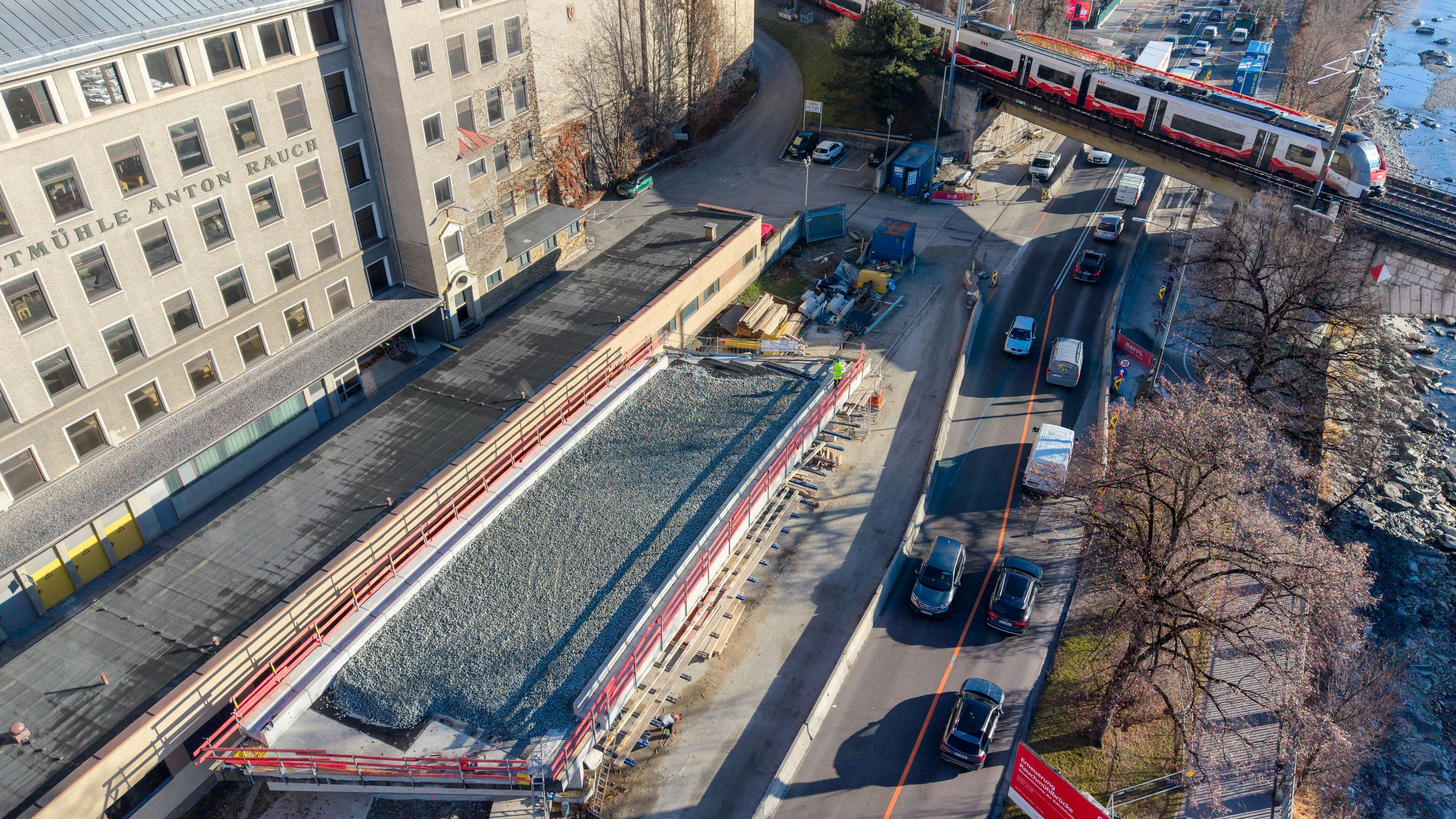 defaultVorne links vor dem Gebäude der Rauchmühle das vorgefertigte neue Tragwerk, bereits mit Gleisschotter, dahinter die Bestandsbrücke mit Zug