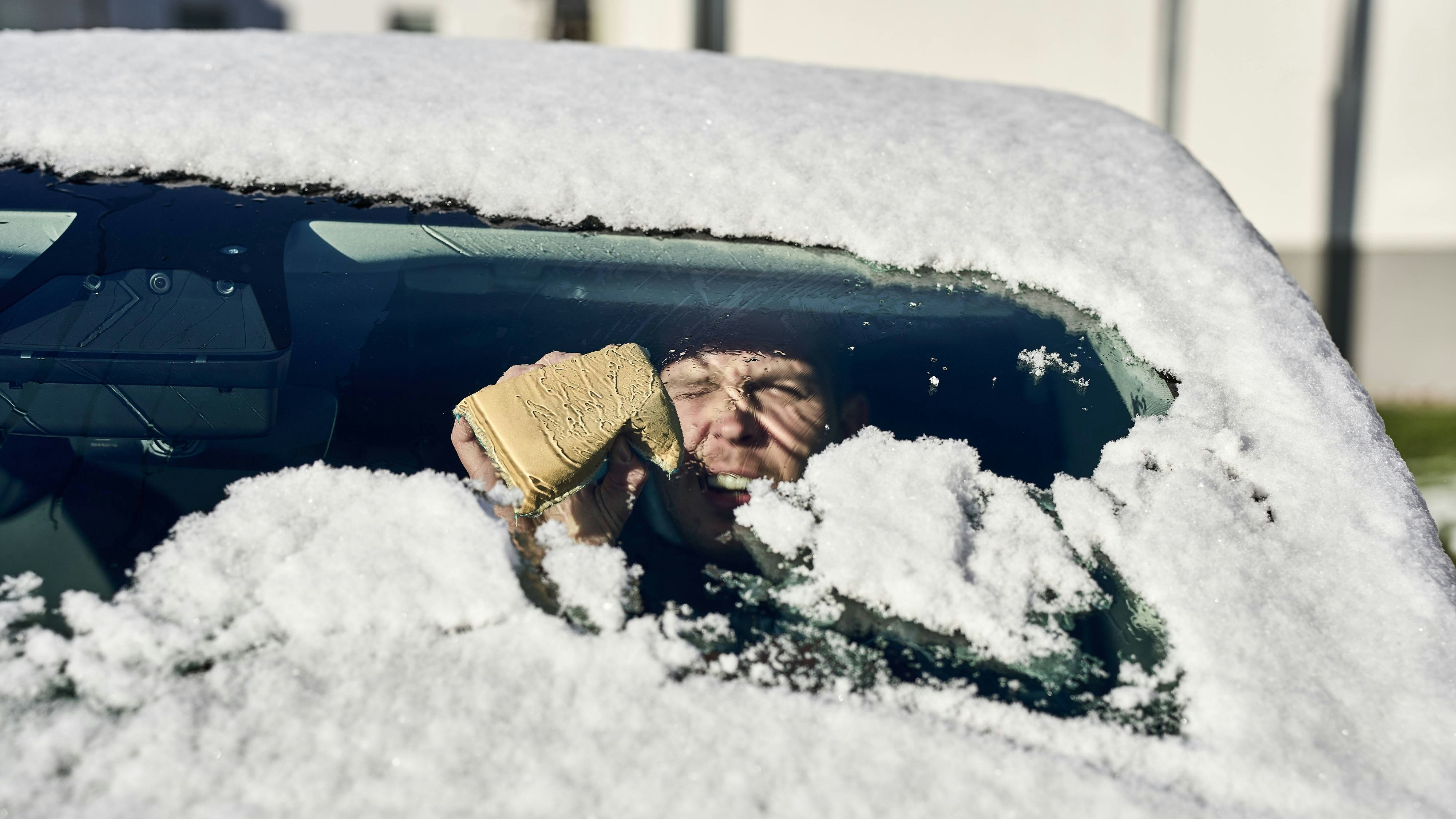 Bavaria, Germany - November 22, 2024: A man sits in a car with snow-covered windows and uses a sponge to clear the steamed-up windshield. A typical winter situation showing the fight against cold and ice *** Ein Mann sitzt in einem Auto mit zugeschneiten Scheiben und nutzt einen Schwamm, um die beschlagene Frontscheibe freizulegen. Eine typische Wintersituation, die den Kampf gegen Kälte und Eis zeigt