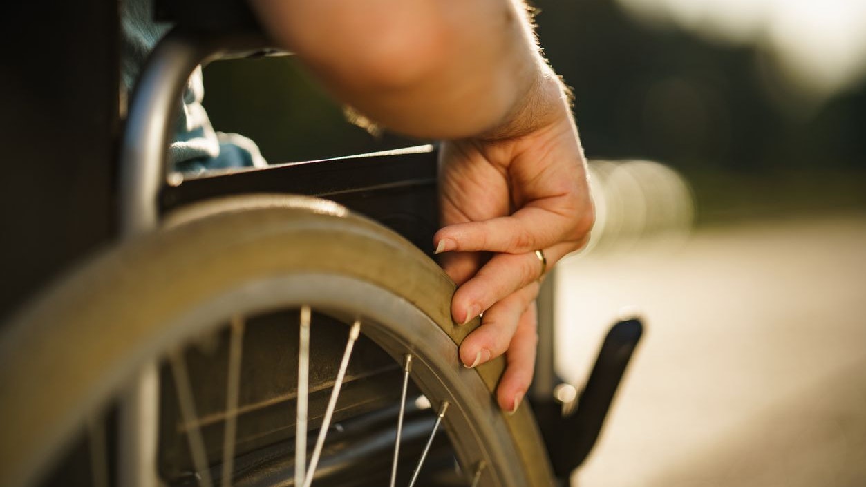 Close up women's hand pushing wheelchair during sunny day in public park